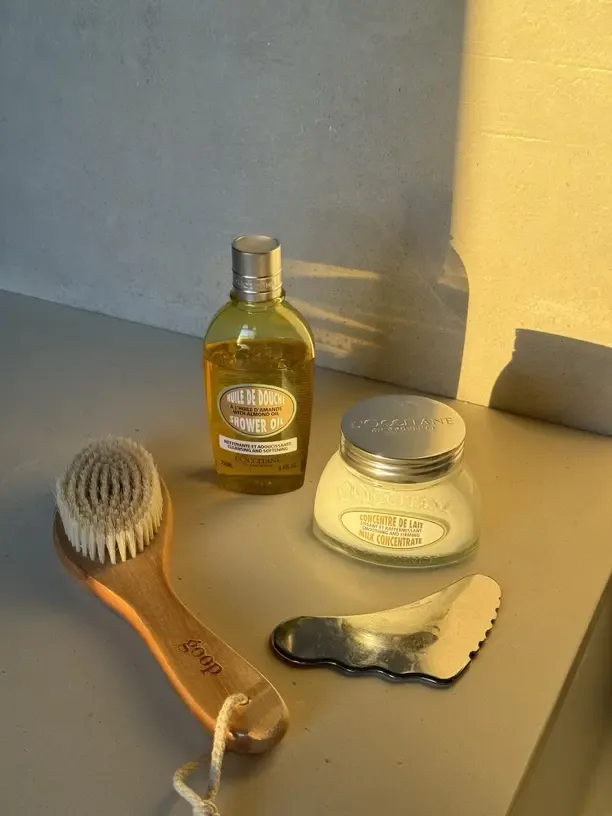 body care routine with a dry brush, body oil and body cream in sunlight