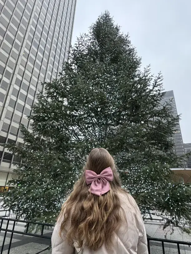 Christmas hair idea with long wavy hair and a satin bow in front of a big Christmas tree.