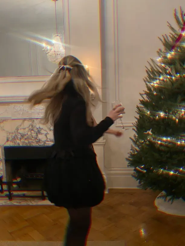 Christmas outfit idea with a girl in a black dress and hair bow twirling beside a lit Christmas tree.