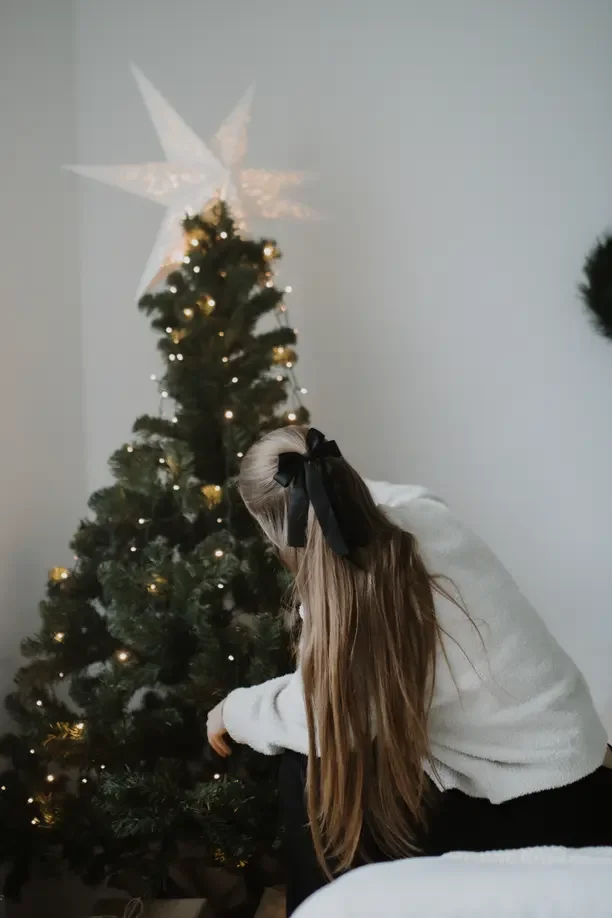 Christmas tree star idea with a girl placing a white star topper on the Christmas tree.