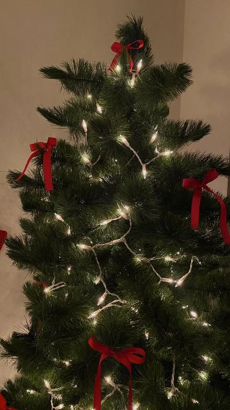 Christmas wallpaper for iPhone idea with a lit Christmas tree decorated with red bows.