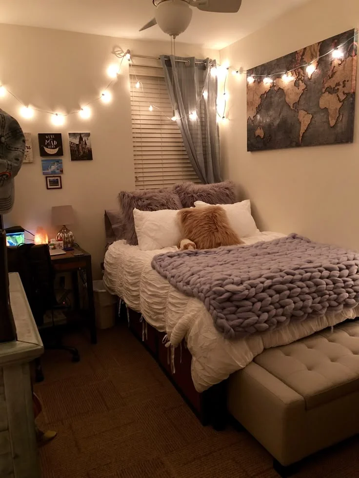 Cozy college apartment bedroom with string lights, a purple throw and pillows on the bed