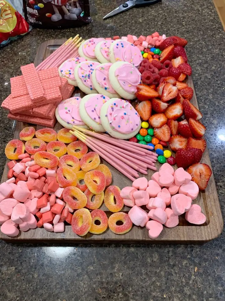 Pink color board with frosted cookies, pink candy, strawberries and marshmallows