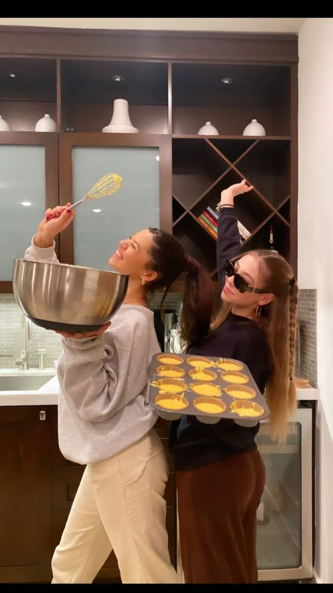 Two friends laughing together while baking in a kitchen
