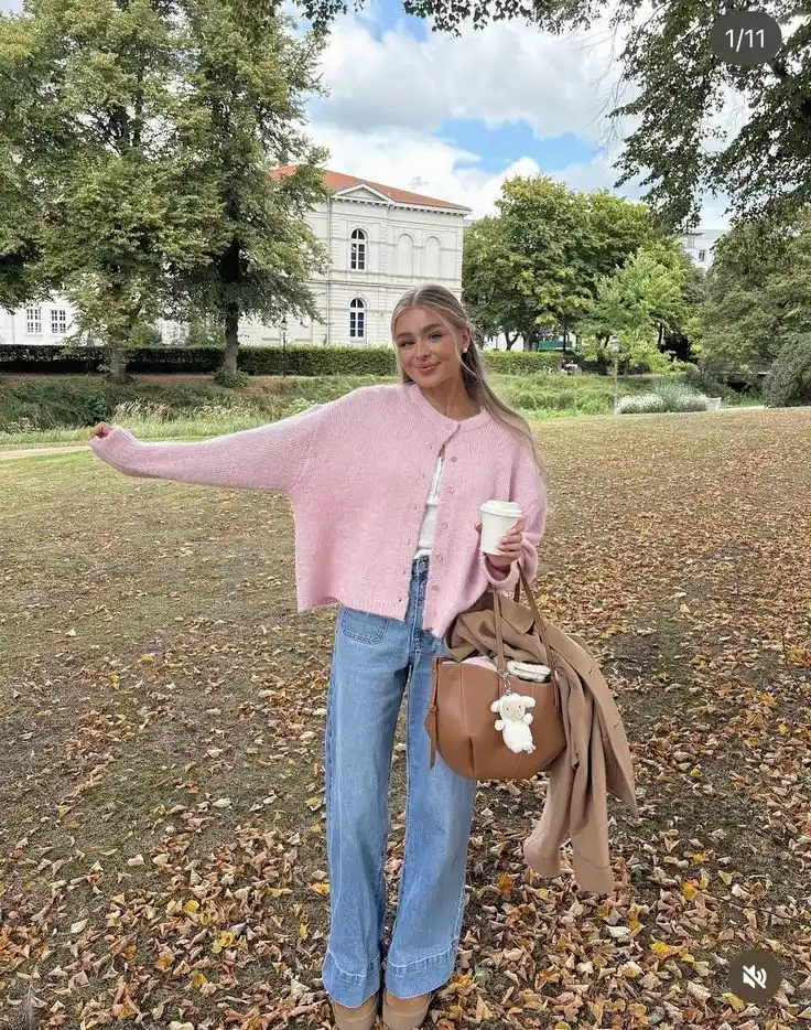 Woman in a pink sweater and jeans holding a bag in a fall park
