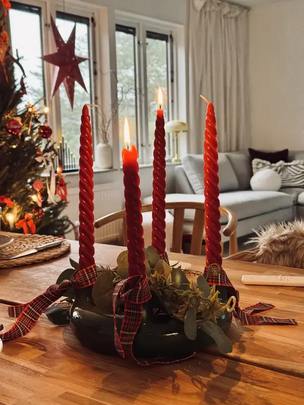 Rustic Christmas tablescape with tall red taper candles, greenery and a plaid ribbon on a wood dining table.